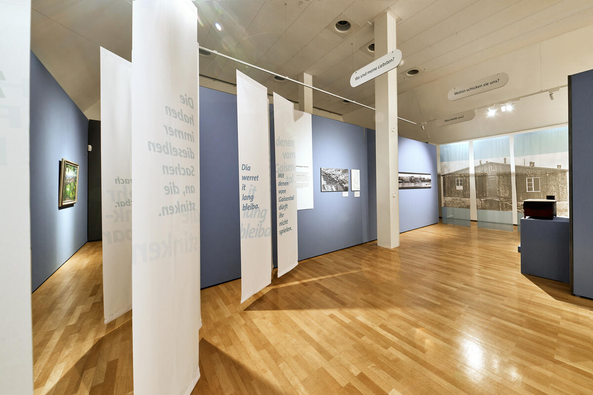 Bild vergrößern: Ausstellungsraum mit von der Decke hängende Bahnen, die historische Zitate zeigen.