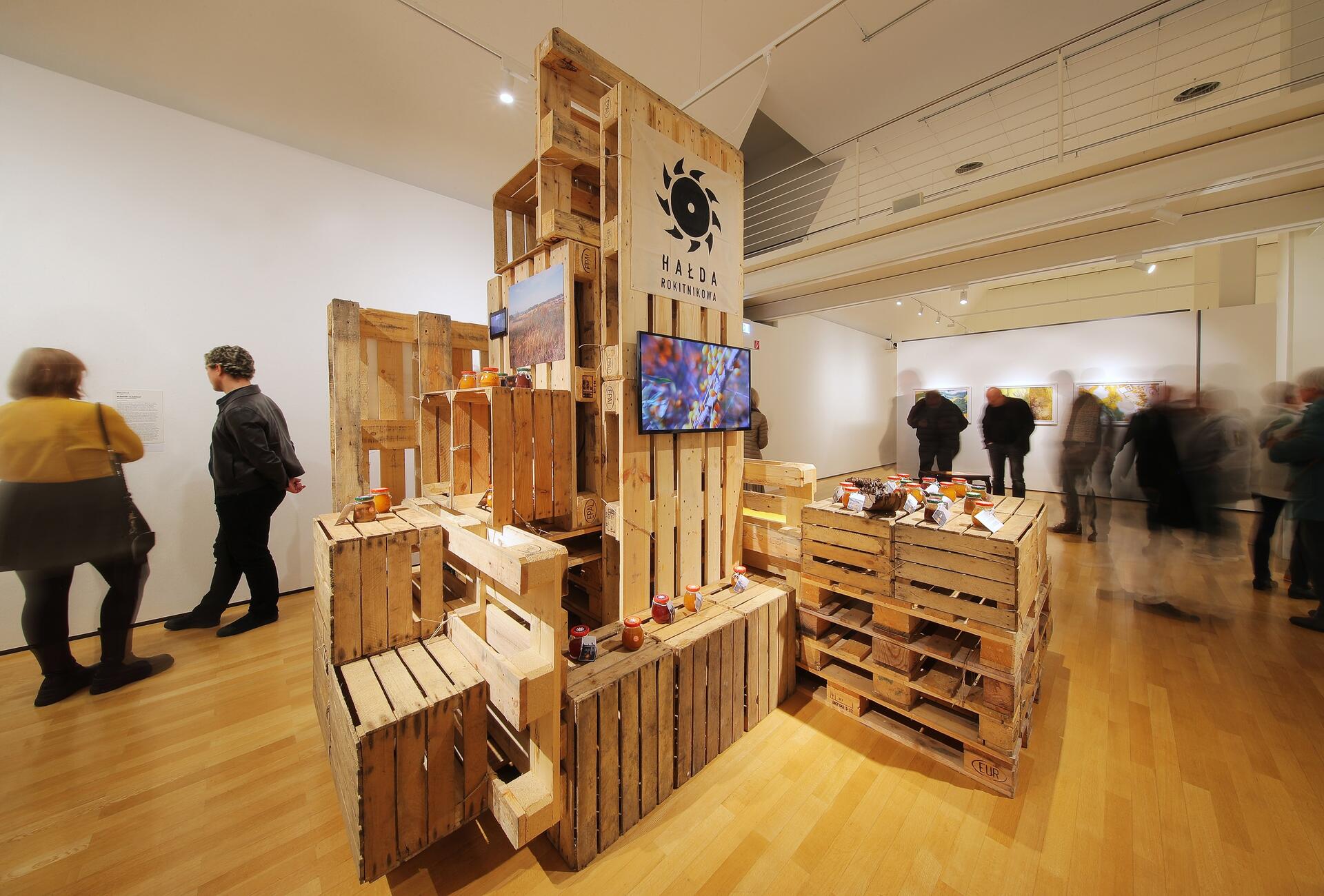Installationsansicht der Ausstellung "Konsum in der Kunst" mit dem Werk "Seaberry Slagheap" von Diana Lelonek, das aus übereinandergestapelten Europalletten besteht. 