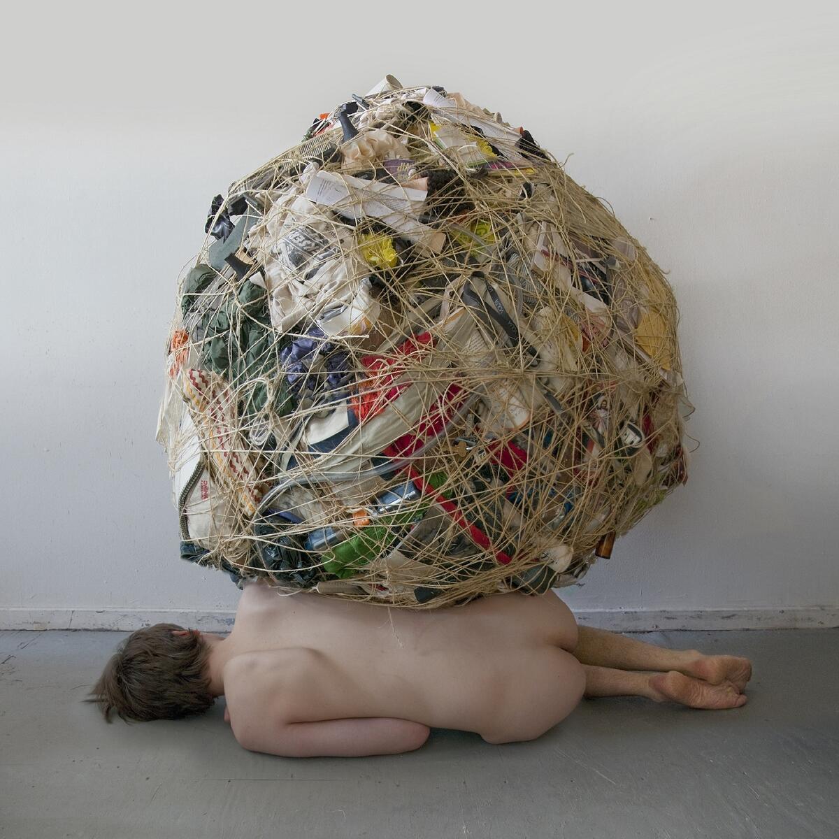 Bild vergrößern: Fotografie von Mary Mattingly mit einer liegenden, unbekleideten Person, deren Besitz in einem geschnürten Bündel auf ihr liegt.