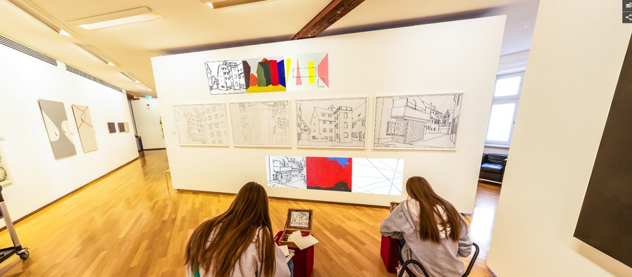 Bild vergrößern: Schülerinnen sitzen vor einer Wand mit Zeichnungen und zeichnen.